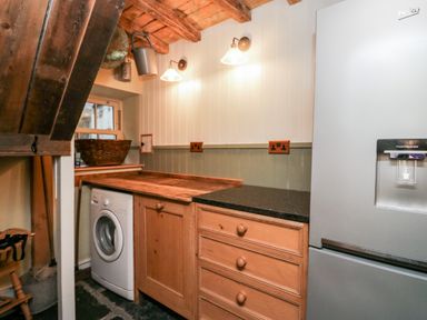 A kitchen area with wooden cabinets a washing machine a basket on the counter and a refrigerator with a water dispenser at Eden Vale in Broughton-In-Furness
