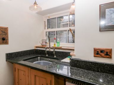 A kitchen sink with a faucet on a black countertop under a window at Eden Vale in Broughton-In-Furness