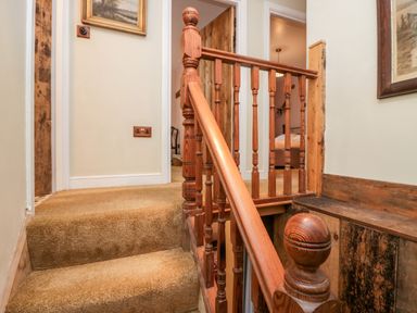 A staircase with wooden railings and beige carpet leading to a hallway with open doors at Eden Vale in Broughton-In-Furness