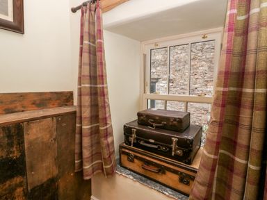 A window with three stacked vintage suitcases on the sill and plaid curtains on each side at Eden Vale in Broughton-In-Furness