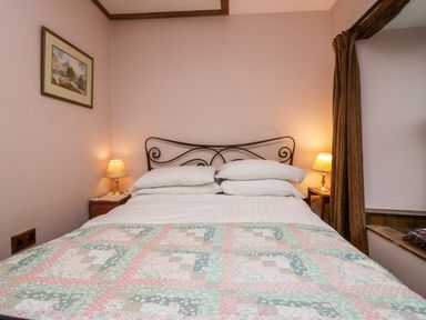 A bedroom with a bed with white pillows and a patterned quilt with bedside tables and lamps at Eden Vale in Broughton-In-Furness