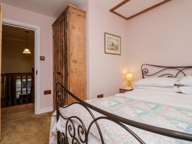 A bedroom with a metal framed bed a wooden wardrobe a bedside lamp and a framed picture on the wall at Eden Vale in Broughton-In-Furness