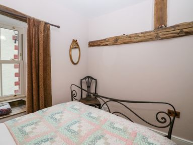 A bedroom with a patterned quilt on the bed a black metal bed frame a wooden chair an ornate oval mirror and a window with brown curtains at Eden Vale in Broughton-In-Furness
