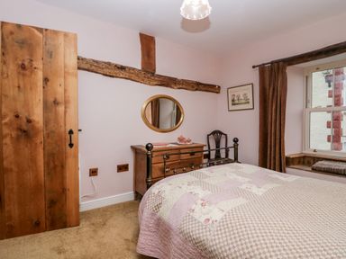 A bedroom with a wooden door a bed a wooden dresser with a round mirror above and a window with curtains at Eden Vale in Broughton-In-Furness
