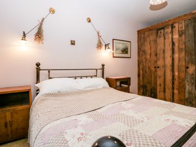 A bedroom with a bed and patchwork quilt two bedside tables wooden wardrobe and wall lamps at Eden Vale in Broughton-In-Furness