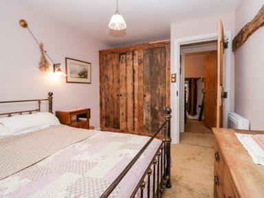 A bedroom with a metal bed frame wooden wardrobe wooden chest of drawers and an open door at Eden Vale in Broughton-In-Furness