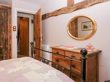 A bedroom with a metal bed frame a wooden dresser with a round mirror and wooden doors at Eden Vale in Broughton-In-Furness
