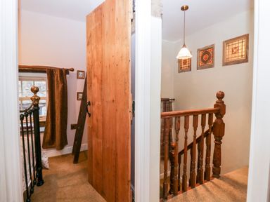 A wooden door between a bedroom with a metal bed and a stairwell with wooden railing and stained glass windows at Eden Vale in Broughton-In-Furness