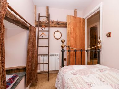 A bedroom with a metal bed frame a patchwork quilt wooden door ladder with hangers and a small round mirror at Eden Vale in Broughton-In-Furness