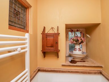 A bathroom corner with stained glass window wooden cabinet and flowers in a pitcher at Eden Vale in Broughton-In-Furness