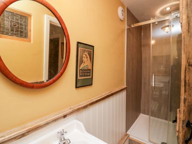A bathroom with a round mirror above a sink and a glass shower enclosure at Eden Vale in Broughton-In-Furness