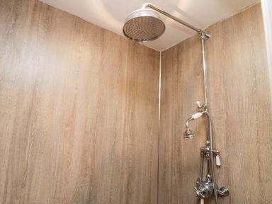 A shower area with a large round shower head and a handheld shower head in a wood paneled shower at Eden Vale in Broughton-In-Furness