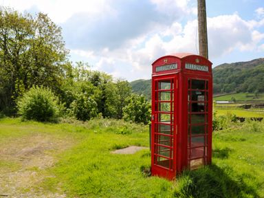 A red telephone box near a wooden pole surrounded by grass and trees at Eden Vale Broughton-In-Furness