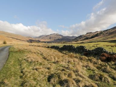 A rural landscape with a narrow road grassy fields stone walls and hills in the distance at Eden Vale in Broughton-In-Furness
