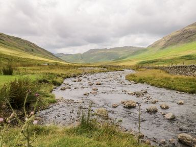 A mountain valley with a rocky stream flowing through grass and a stone wall along the right side at Eden Vale in Broughton-In-Furness