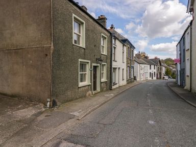 A street with terraced houses and a narrow sidewalk under a partly cloudy sky at Eden Vale in Broughton-In-Furness
