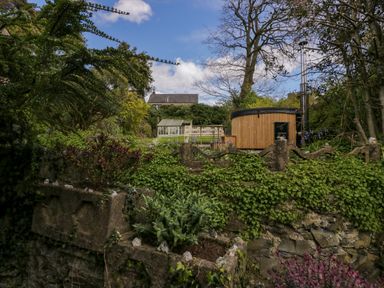 A garden with a wooden hot tub and a greenhouse surrounded by greenery and stone walls at Eden Vale in Broughton-In-Furness