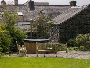 A garden with metal benches and a covered hot tub near stone buildings at Eden Vale in Broughton-In-Furness