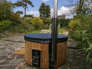 A covered wooden hot tub on a stone patio in a garden with benches and greenery at Eden Vale in Broughton-In-Furness