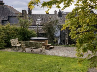A garden with metal benches and a hot tub on a stone patio with houses in the background at Eden Vale in Broughton-In-Furness