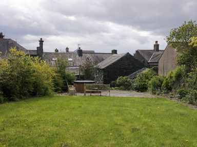 A garden with a grassy lawn stone patio benches and surrounding houses at Eden Vale in Broughton-In-Furness