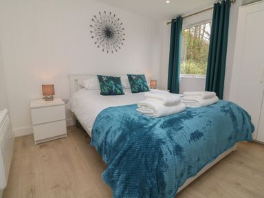 A bedroom with a double bed two bedside tables with lamps a window with curtains and a wardrobe at Cassia in Kilkhampton