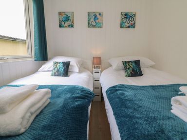 A bedroom with two single beds with blue throws and pillows and sea-themed wall art at Cassia in Kilkhampton