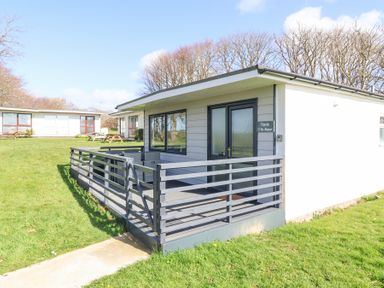 A single-story cottage with a fenced porch and outdoor seating on a grassy area at Cassia in Kilkhampton