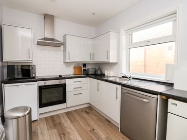 A kitchen with white cabinets black countertops a stainless steel oven microwave dishwasher and a window at 46 The Promenade in Withernsea