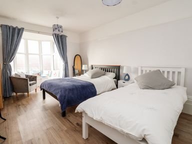 A bedroom with two beds a chair a full length mirror and curtains at 46 The Promenade in Withernsea