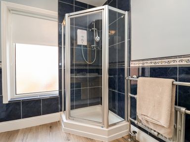 A bathroom shower enclosure with glass doors and blue tiled walls at 46 The Promenade in Withernsea