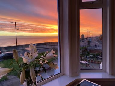A view of a sunset over the sea through a window with white lilies on the windowsill at 46 The Promenade in Withernsea