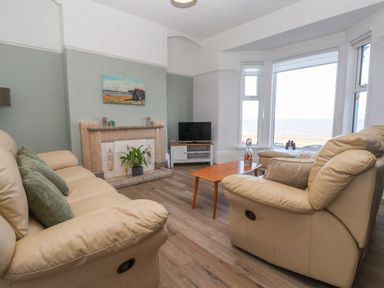 A living room with beige sofas a wooden coffee table a fireplace and a television near large windows overlooking the sea at 46 The Promenade in Withernsea