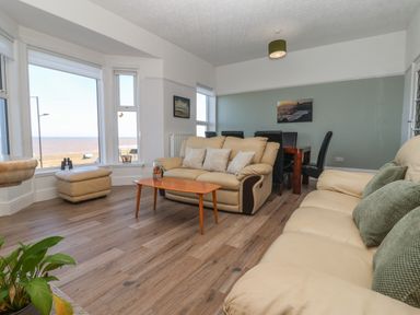 A living room with beige sofas a wooden coffee table a dining table with black chairs and large windows overlooking the sea at 46 The Promenade in Withernsea