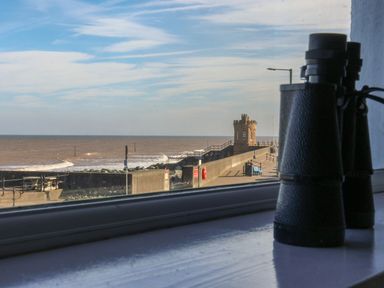 A view of a sea wall and a small tower seen through a window with binoculars on the windowsill at 46 The Promenade in Withernsea
