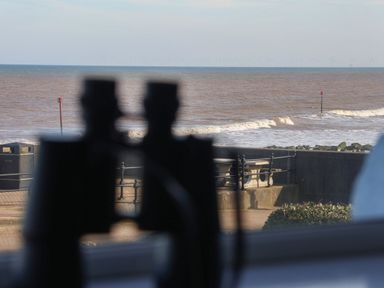 A view of the sea with waves and wind turbines on the horizon seen through a window with binoculars in the foreground at 46 The Promenade in Withernsea