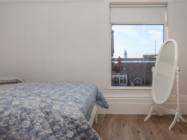 A bedroom with a bed covered by a floral quilt and a freestanding mirror near a window at 46 The Promenade in Withernsea
