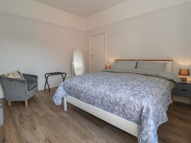 A bedroom with a bed covered with a floral quilt two bedside tables with lamps an armchair a full-length mirror and a luggage rack at 46 The Promenade in Withernsea
