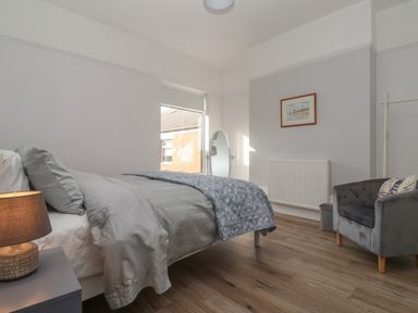 A bedroom with a bed a bedside lamp a chair a standing mirror and a framed picture at 46 The Promenade in Withernsea