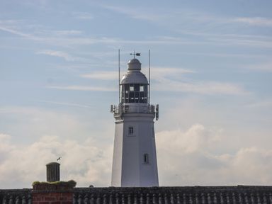 A lighthouse behind rooftops under a partly cloudy sky at 46 The Promenade in Withernsea
