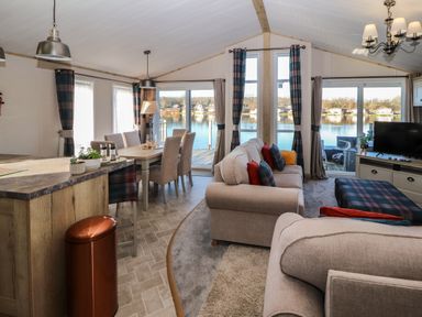 A living and dining area with sofas dining table chairs and windows overlooking a lake at Gressingham 7 in Warton near Carnforth
