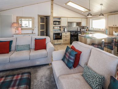 An open plan living room and kitchen with sofas red and patterned cushions and a kitchen island with stools at Gressingham 7 in Warton near Carnforth