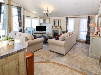 A living room with two beige sofas a plaid ottoman a television and windows with plaid curtains at Gressingham 7 in Warton near Carnforth