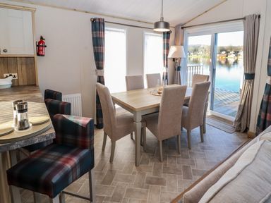 A dining room with a rectangular wooden table six upholstered chairs and stools by a kitchen counter at Gressingham 7 in Warton near Carnforth