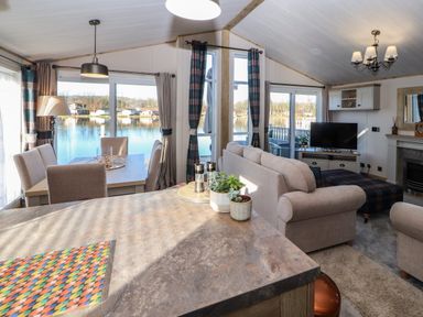 A living and dining area with sofas a TV dining table and windows overlooking a lake at Gressingham 7 in Warton near Carnforth