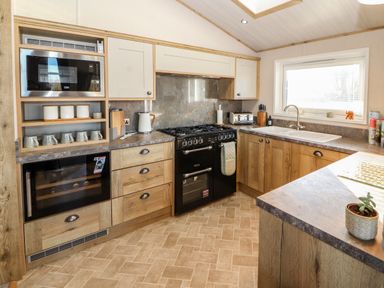 A kitchen with wooden cabinets a black stove a sink a microwave and countertop appliances at Gressingham 7 in Warton near Carnforth
