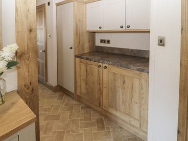 A hallway with wood cabinets and stone countertop with a wooden door and flowers in a vase at Gressingham 7 in Warton near Carnforth
