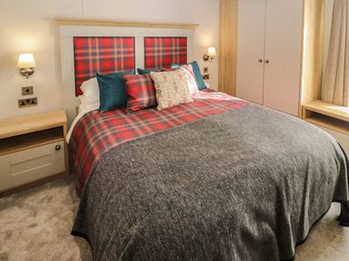 A bedroom with a double bed with red plaid bedding blue and patterned pillows bedside tables and wall lamps at Gressingham 7 in Warton near Carnforth