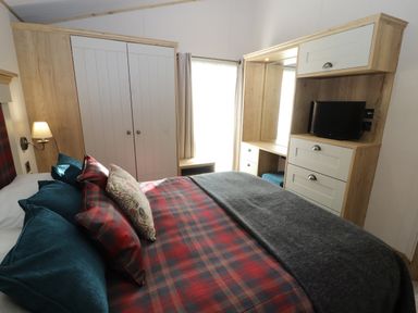 A bedroom with a bed with pillows and blankets a wardrobe a wall lamp a window and a dresser with a television at Gressingham 7 in Warton near Carnforth