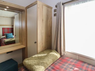 A bedroom with a wooden wardrobe a bed with a plaid bedspread and a textured blanket a mirror and a window with curtains at Gressingham 7 in Warton near Carnforth